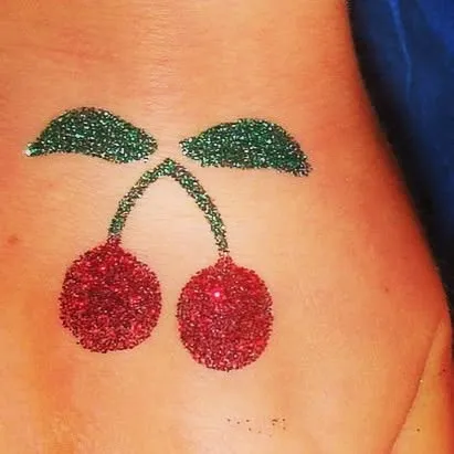 A fun and fruity cherry glitter tattoo. This is a cute and playful design that adds a pop of color.
