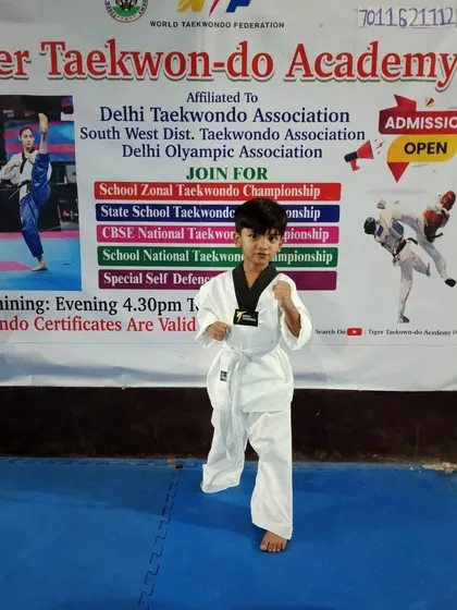 A young student in his white belt 'dobok' (uniform), practicing his fighting stance in front of our academy banner.