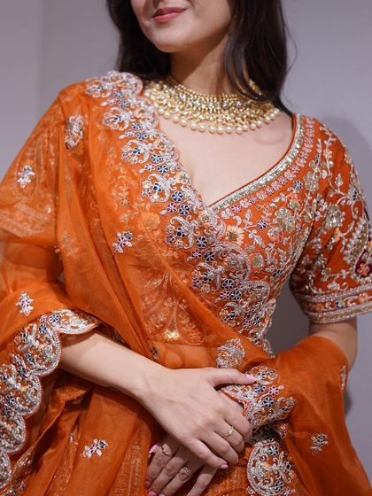 A close-up of a stunning orange lehenga, showing the intricate multi-colored embroidery on the blouse. The craftsmanship is simply exquisite.