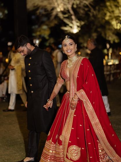 A happy bride walking with her groom. Her minimal makeup and classic red lehenga create a timeless and elegant look.