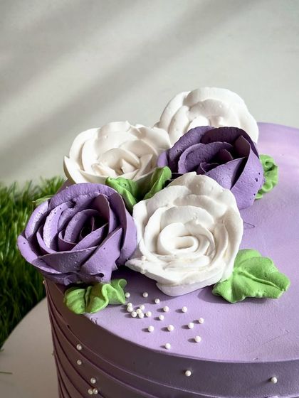 A close-up of the hand-piped whipped cream florals on our purple cake. Each petal is carefully crafted to create a stunning, edible bouquet.