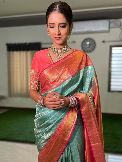 This client is wearing a beautiful sea-green Kanchivaram with a pink border, paired with a contrasting peach-colored blouse with delicate sleeve embroidery.