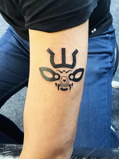 A bold tribal-style mask tattoo. This design uses solid black ink to create a powerful and fierce look, drawing on ancient symbolism.