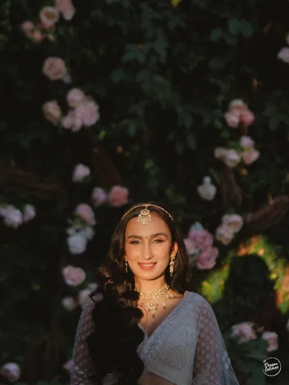 The bride's beautiful smile, illuminated by a perfect ray of sunlight against a wall of flowers. A moment of pure, natural radiance.