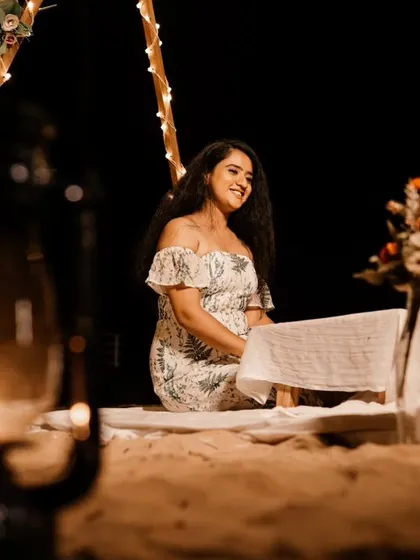 A solo portrait of the bride-to-be smiling during a romantic nighttime beach setup, with lanterns and fairy lights creating a warm, inviting glow.