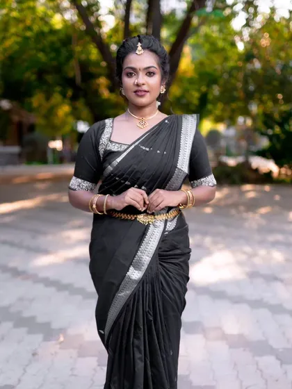 A full-length shot of the model in a black saree, looking elegant and poised. The makeup is timeless and suits her traditional attire perfectly.