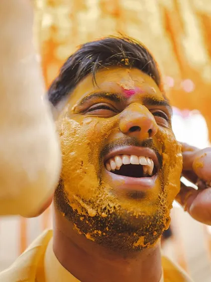 A close-up of a groom's face covered in turmeric during his Haldi. The pure joy and laughter in this moment are what it's all about.