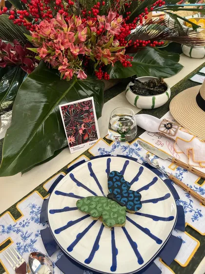 A vibrant place setting from a brunch for Farm Rio, featuring butterfly-shaped cookies on a hand-painted plate. The entire setup reflects the brand's colorful, tropical aesthetic.