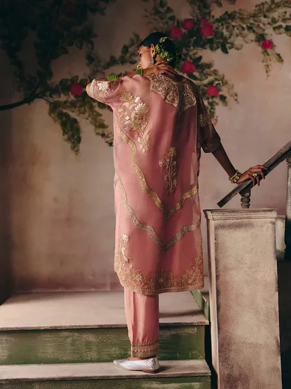 Blush pink, golden threads, and endless beauty. This model ascends a staircase in a stunning kurta set with wavy gold embroidery.