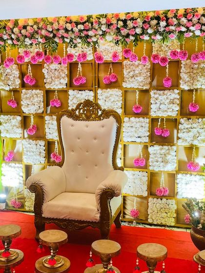 A beautiful pink and white themed backdrop for a baby shower. The checkerboard design is made with panels of white flowers, accented by hanging pink floral tassels for a delicate and feminine touch.