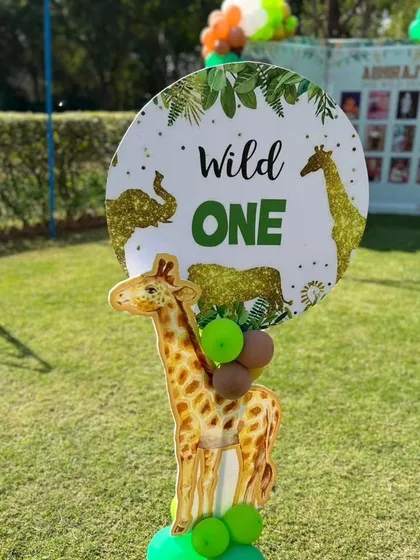 A "Wild One" themed sign with a giraffe cutout, perfect for a first birthday party in a garden setting.