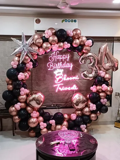 A glamorous 34th birthday setup right in the living room. We designed a full balloon ring with rose gold, black, and pink balloons, a personalized neon sign with the birthday girl's name, and foil number balloons.