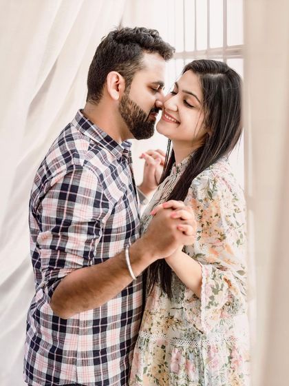 An intimate and gentle moment captured by a window. The soft, natural light and the couple's tender expressions create a warm and romantic photo with a timeless feel.