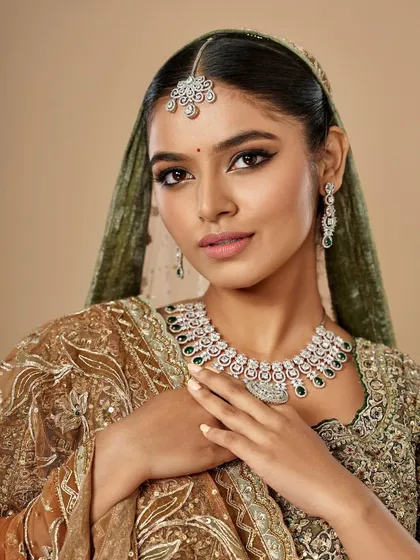 This bride is wearing a unique olive and gold lehenga. The makeup features a warm, bronzed smokey eye and a soft pink lip to complement the earthy tones of her outfit.