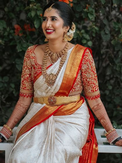 A full view of Chaitra's muhurtham outfit. The rich embroidery on the blouse sleeves balances the traditional temple jewelry and the classic elegance of the white silk saree.