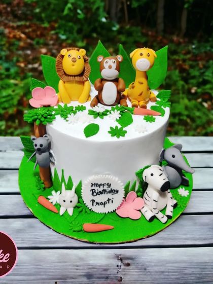 A charming jungle animal cake set on a background of natural greenery. This cake features a lion, monkey, and giraffe, perfect for a nature-themed party.
