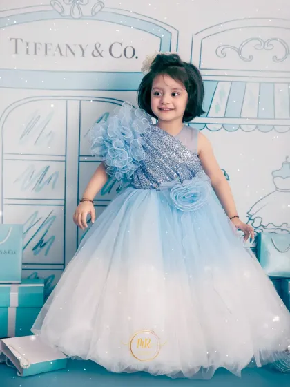 A glamorous toddler photoshoot with a "Tiffany & Co." theme. She looks like a little star in her sequined blue gown against the illustrated storefront backdrop.
