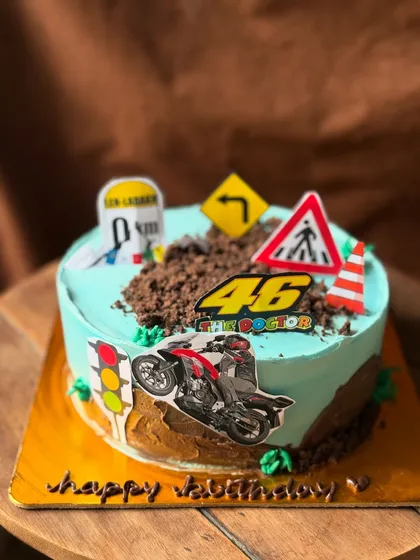 A non-fondant cake for a bike lover, featuring road signs and a motorcycle topper on a bed of chocolate "dirt".