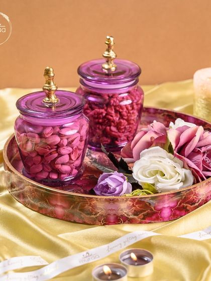 This vibrant Karwa Chauth hamper features purple glass jars and a matching decorative tray, filled with premium nuts and adorned with flowers.