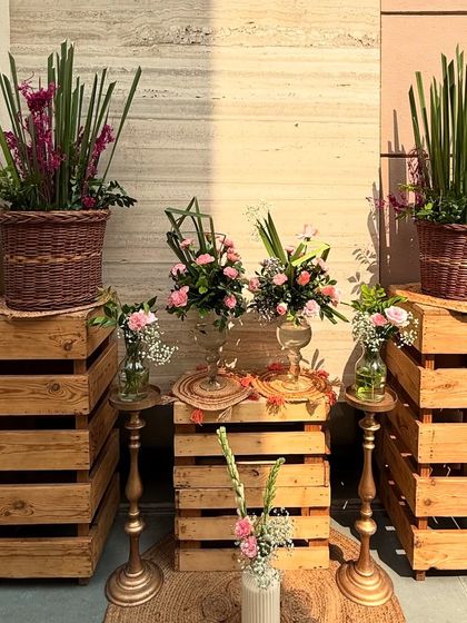 A rustic and charming decor element for an 80th birthday party. We used wooden crates, wicker baskets, and brass stands to display beautiful pink floral arrangements, adding texture and warmth to the space.