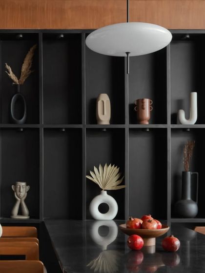 A close-up of the black veneer display cabinet, filled with minimalist ceramic and decorative objects. This feature adds functional storage and a personal touch to the dining space.