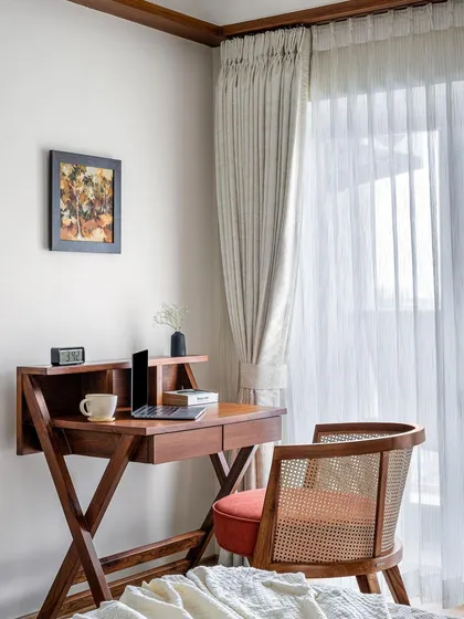The primary room in 'Gulmohar' includes this classic wooden study desk with crisscross legs, paired with a comfortable cane-back chair.
