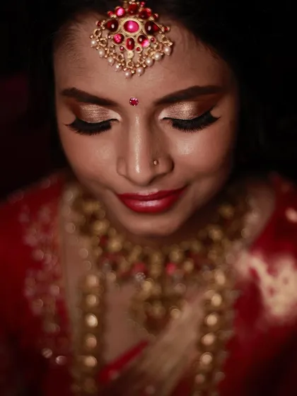 A close-up shot focusing on the rich, golden eye makeup and bold red lip, a classic combination for a traditional Indian bridal look.