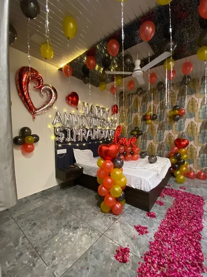 For this anniversary surprise, I created a full room transformation. The setup includes a custom foil balloon message with the couple's names, a romantic rose petal pathway leading to the bed, and a mix of red, yellow, and black balloons for a vibrant, celebratory feel.