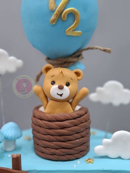 A close-up of the adorable teddy bear figurine peeking out of the hot air balloon basket.