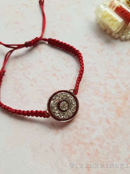 The red crystal Rakhi, shown here with its Roli-Chawal holder. The braided red thread is adjustable and comfortable to wear.