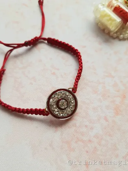 The red crystal Rakhi, shown here with its Roli-Chawal holder. The braided red thread is adjustable and comfortable to wear.