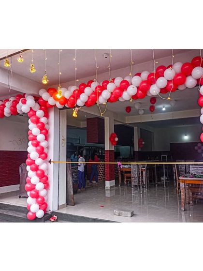 A grand entrance for a hotel's opening ceremony. This large red and white spiral balloon arch, accented with hanging incandescent bulbs, creates a celebratory and professional welcome for guests and patrons.