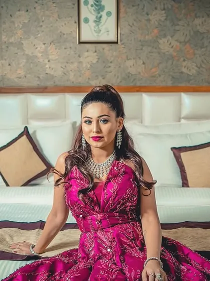 A full-length portrait of the bride seated on a bed, showcasing her magnificent engagement gown in a relaxed, pre-ceremony setting.