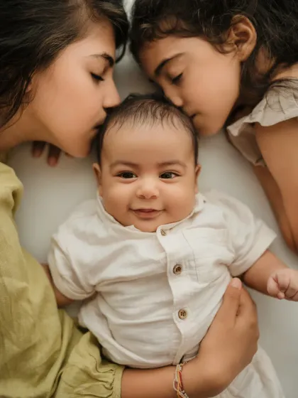 An overhead shot of two sisters kissing their baby brother's head. A sweet and artistic way to capture a sibling portrait.