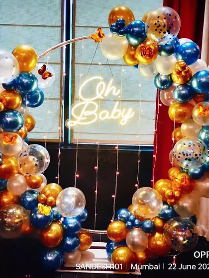 An elegant "Oh Baby" balloon ring in blue and gold. This setup is perfect for a sophisticated baby shower, featuring a neon sign and confetti balloons.