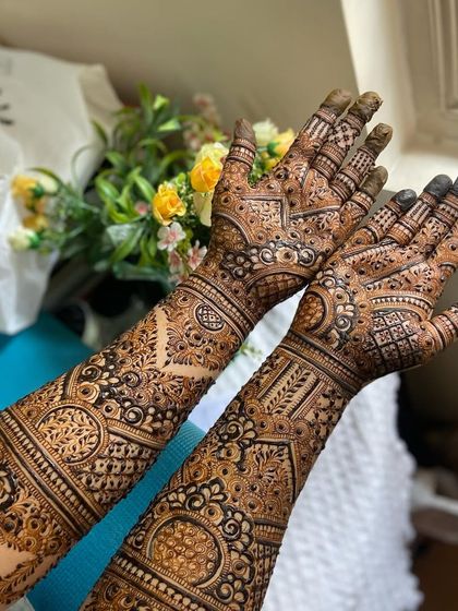 A full view of both arms, showcasing the complete bridal henna from fingertips to forearm.
