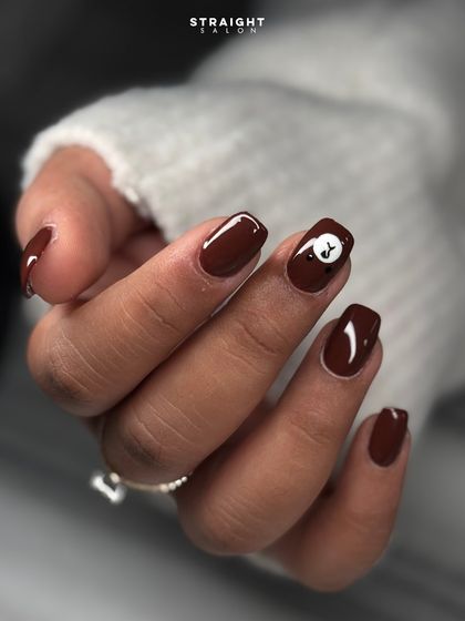 A fun and playful manicure featuring a rich brown polish with a cute, hand-painted teddy bear accent nail.