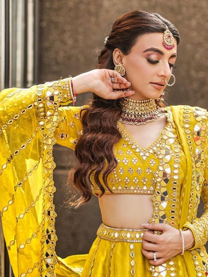 A close-up portrait of the bride in her vibrant yellow Mehendi outfit, looking down with a gentle smile.