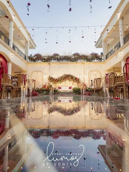 A breathtaking reflection shot of a regal wedding ceremony setup. The mirrored aisle perfectly reflects the grand architecture, chandeliers, and elegant decor.