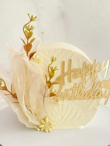 An artistic and modern birthday cake with a textured finish, delicate sail decorations, and a gold topper.