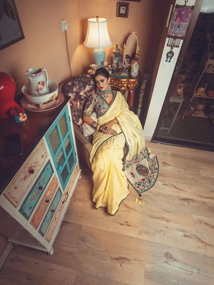 An overhead shot from the vintage-themed ethnic shoot. The model is styled in the yellow saree with an embroidered jacket blouse, showcasing how the outfit drapes beautifully even when seated.