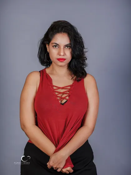 A simple, strong stance against a neutral grey background. This studio shot isolates the subject, letting the vibrant red top and her direct gaze command the frame.