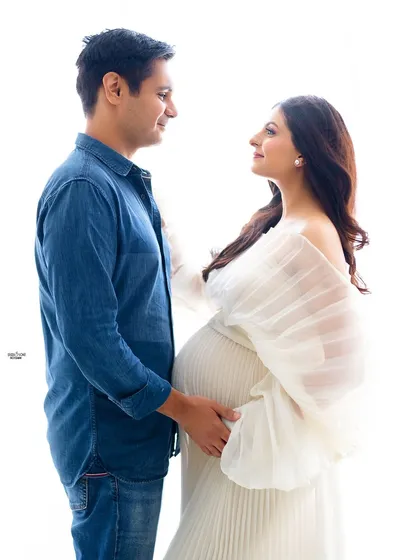 A lovely high-key portrait of a couple ready to welcome their new baby. The flowing white gown and the partner's casual denim shirt create a relaxed and happy vibe.