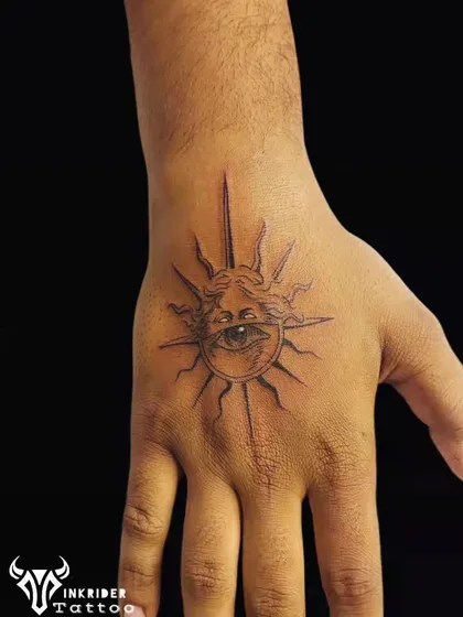 A watchful eye within a sun, tattooed on the hand. This fine-line piece is a symbol of protection and powerful energy, placed in a highly visible spot.