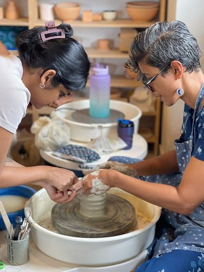 A close up of hands on guidance, as I help a student with the delicate process of shaping her piece on the wheel.