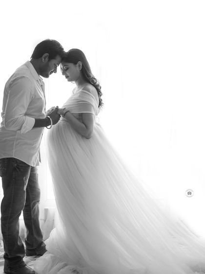 A soft, high-key black and white portrait of a couple. The bright background creates a dreamy, ethereal feel, focusing on their tender connection.