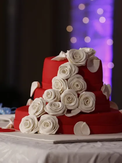 A shot of a magnificent three-tiered red wedding cake adorned with white sugar roses.