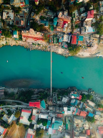 A perfect top-down drone shot of Laxman Jhula in Rishikesh. This symmetrical photo shows the bridge spanning the turquoise Ganga, connecting the two sides of the bustling town.