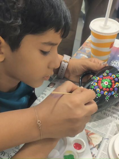 A young boy engrossed in the dot painting process, carefully creating his design on a black mug.