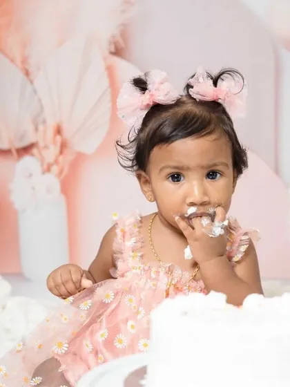 A sweet one-year-old girl enjoying her pink-themed cake smash session. I love capturing these close-ups of their frosting-covered fingers and happy faces.